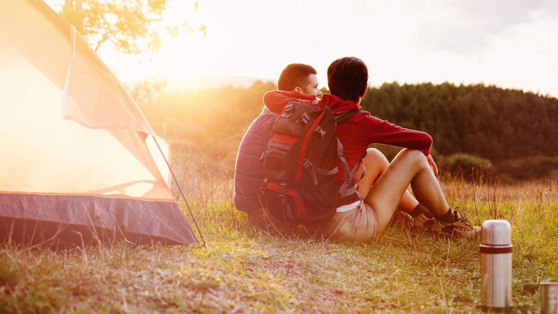 foto de um casal sentado com campo com barraca de camping no por do sol